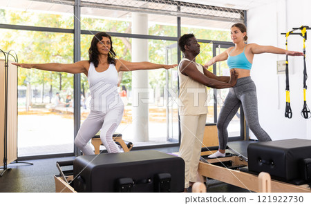 Female pilates trainer helping pilates people during training Female pilates trainer helping pilates people during training 121922730