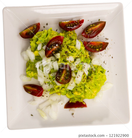 Pile of guacamole on plate, sprinkled with chopped hot onions, decorated with slices of tomatoes 121922900