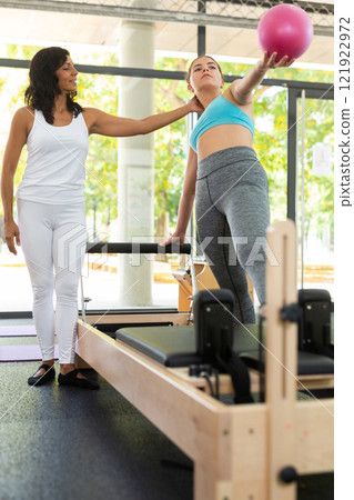 Girl doing exercises in pilates gym with female instructor 121922972