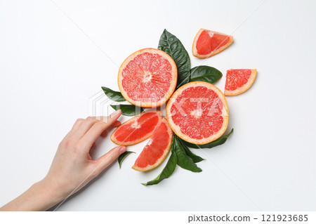 Sliced ripe grapefruits with leaves and female hand on white background, top view 121923685