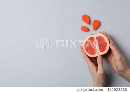 Half of grapefruit in female hands and paper drops on gray background, space for text Half of grapefruit in female hands and paper drops on gray background, space for text 121923688