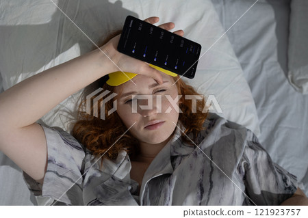 A Young Woman Who Is Feeling Unwell While Using Her Smartphone While in Bed and Resting 121923757