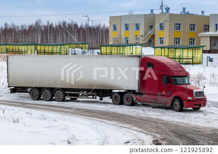Red long-distance bonnet truck with a white semitrailer in the countryside at winter 121925892