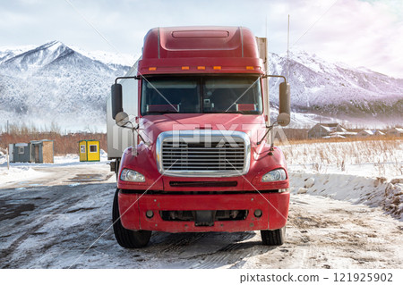 Front view of the red long-distance bonnet truck with a white semitrailer at winter on the background of high scenic mountains Front view of the red long-distance bonnet truck with a white semitrailer at winter on the background of high scenic mountains 121925902
