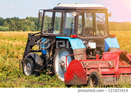 Modern wheeled agricultural tractor with harvesting equipment on an field 121925914