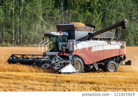 Modern combine harvester working in the field on a clear sunny day Modern combine harvester working in the field on a clear sunny day 121925929