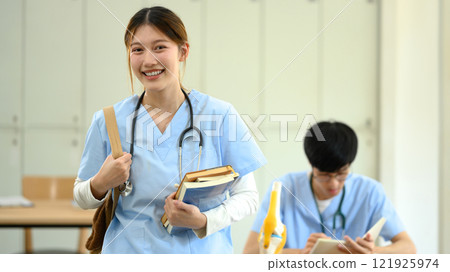 Smiling medical student in scrubs carrying books heading to class Smiling medical student in scrubs carrying books heading to class 121925974