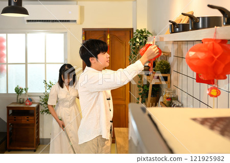 Young man decorating home with red ornaments during Chinese New Year celebration Young man decorating home with red ornaments during Chinese New Year celebration 121925982
