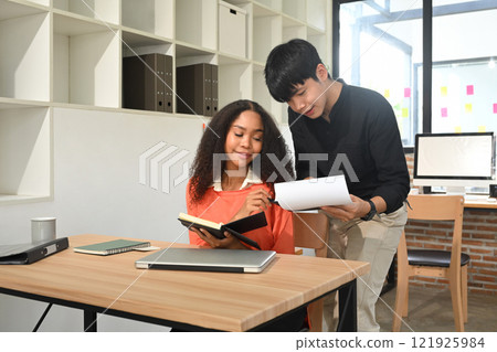 Young entrepreneurs collaborating over business reports at modern workplace Young entrepreneurs collaborating over business reports at modern workplace 121925984