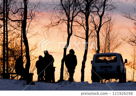 Picnic in nature by car at the top of a mountain in winter at sunset, silhouettes of people and a car on a yellow background Silhouetted figures stand against a stunning and beautiful sunset at days 121926298