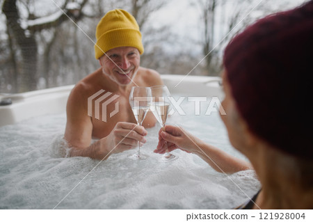 Senior couple bathing in hot tub during cold winter day, toasting with champagne. Romantic wellness getaway with spa during Valentine's weekend. Senior couple bathing in hot tub during cold winter day, toasting with champagne. Romantic wellness getaway with spa during Valentine's weekend. 121928004