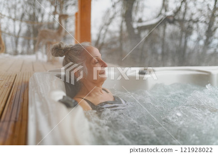 Senior woman bathing in hot tub during cold winter day, enjoying peaceful moment. 121928022