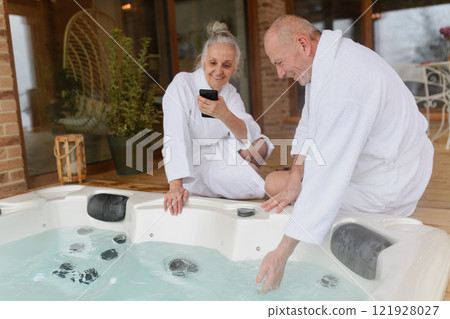 Older man checking water temperature in hot tub with hand. Romantic wellness getaway for senior couple. Valentine's weekend. 121928027