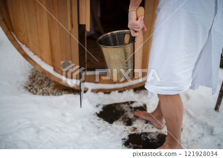 Older man entering small sauna, carrying bucket of water to create steam. Winter Spa weekend getaway for elderly people. Older man entering small sauna, carrying bucket of water to create steam. Winter Spa weekend getaway for elderly people. 121928034
