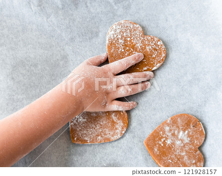 Childs hand decorating heart shaped cookies on baking sheet 121928157