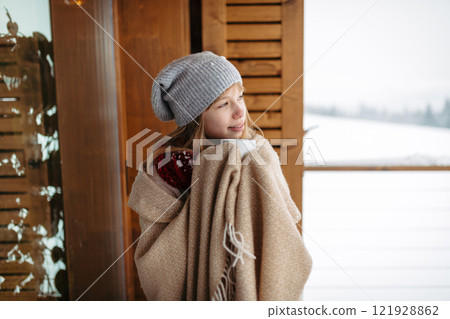 Smilng teen girl bundled in thick blanket holding cup of hot tea standing on balcony during winter day. Smilng teen girl bundled in thick blanket holding cup of hot tea standing on balcony during winter day. 121928862