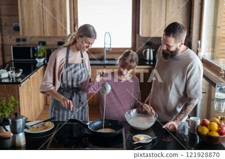 Parents teaching daughter how to make pancakes. Family preparing sweet breakfast in the morning. 121928870