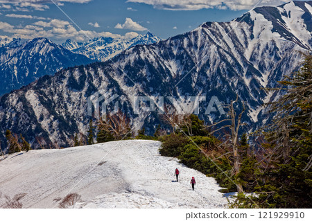 Climbers walking along the snow-covered southern ridge of Mount Jigatake and a view of the Yari and Hotaka mountain ranges 121929910