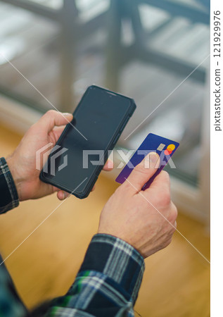man holds smartphone in one hand and a credit card, preparing to make payment. High quality photo 121929976