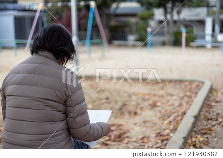 老婦人獨自坐在公園的長椅上，看著一張紙 121930382