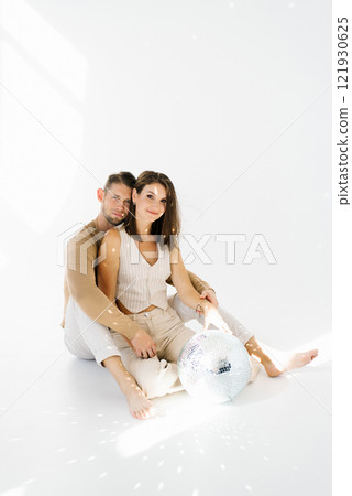 Young happy couple is sitting on the floor with a disco ball in front of them. Scene is playful and fun 121930625