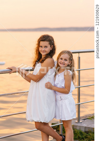 Two child girls are standing on pier by the water, smiling for the camera 121930629