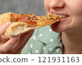 A young woman enjoying a slice of pizza with toppings, smiling and holding it close to her mouth. 121931163