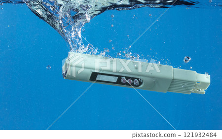 PH acid level test Device tools on quality water on screen. PH acid level tester device tools fall under water splashing splattering with air bubble over blue background isolated 121932484