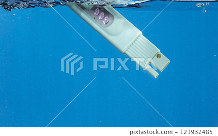 PH acid level test Device tools on quality water on screen. PH acid level tester device tools fall under water splashing splattering with air bubble over blue background isolated 121932485