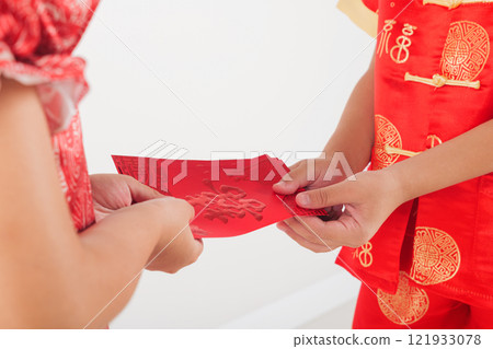 Chinese New Year. Close up hand of Asian little kid sibling boy and girl wear red cheongsam qipao giving red hongbao envelope packet monetary gift 121933078