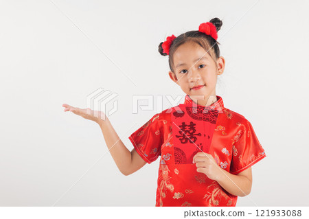 Chinese New Year. Happy Asian Chinese kid girl smile wear red traditional cheongsam qipao dress showing something on hand and holding angpao red packet monetary gift isolated on white 121933088