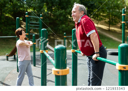 Elderly man doing exercises on a horizontal bar at an outdoor sports ground 121933343