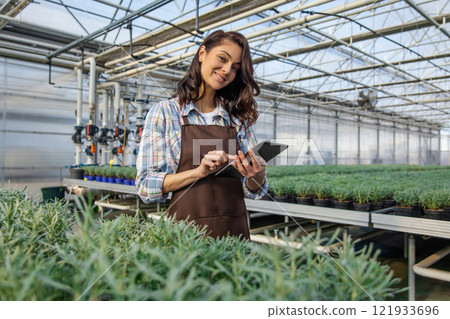 Caucasian young woman working in a greenhouse and looking contented 121933696