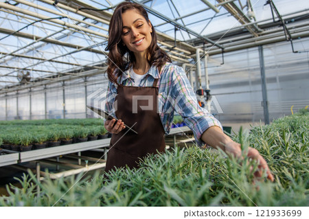 Caucasian young woman working in a greenhouse and looking contented 121933699