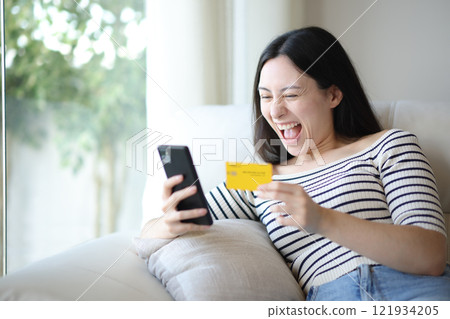 Excited asian woman buying online with card and phone Excited asian woman buying online with card and phone 121934205