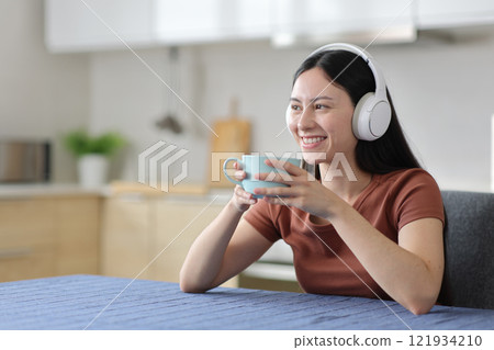 Happy asian woman listening audio and drinking in the kitchen Happy asian woman listening audio and drinking in the kitchen 121934210
