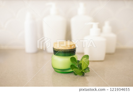 A close-up of a jar of green glass cream with a wooden lid and a twig with leaves A close-up of a jar of green glass cream with a wooden lid and a twig with leaves 121934655
