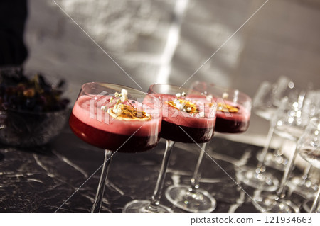 Pink sweet and sour berry cocktails with fluffy foam in elegant long-stemmed glasses. Delicious drinks are decorated with a slice of orange and flowers. Pink sweet and sour berry cocktails with fluffy foam in elegant long-stemmed glasses. Delicious drinks are decorated with a slice of orange and flowers. 121934663