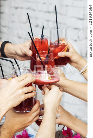 Close-up of male and female hands with elegant glasses. Men and women toast with goblets of delicious fragrant cocktails. Friends clink glasses with tasty drinks. Close-up of male and female hands with elegant glasses. Men and women toast with goblets of delicious fragrant cocktails. Friends clink glasses with tasty drinks. 121934664