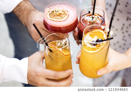 Close-up of male and female hands with elegant glasses. Men and women toast with goblets of colorful cocktails. Friends clink glasses with tasty drinks. Close-up of male and female hands with elegant glasses. Men and women toast with goblets of colorful cocktails. Friends clink glasses with tasty drinks. 121934665