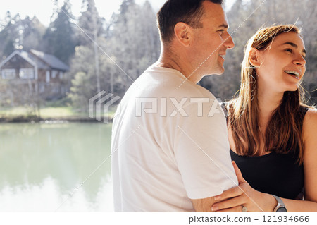 Young married couple hugs in gazebo by lake. Man and woman laugh and enjoy their vacation together 121934666