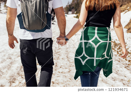 Close-up of young married couple walking along snowy road. Man and woman hold hands and enjoy mountain scenery. View from back. Close-up of young married couple walking along snowy road. Man and woman hold hands and enjoy mountain scenery. View from back. 121934671