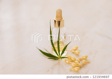 Mockup bottle of cosmetic product with cannabis leaves on beige background. Yellow capsules with whitening moisturizing facial serum with hyaluronic acid with hemp leaf on marble table. Mockup bottle of cosmetic product with cannabis leaves on beige background. Yellow capsules with whitening moisturizing facial serum with hyaluronic acid with hemp leaf on marble table. 121934697