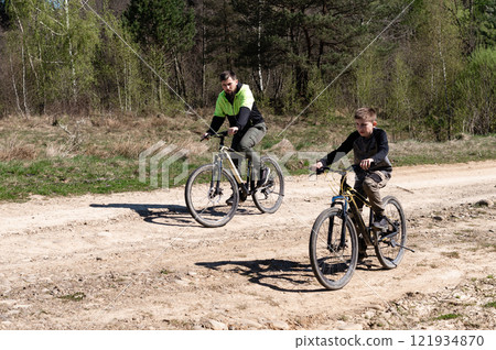 Father and son enjoy a bike ride on a sunny day along a dirt road through the woods. Father and son enjoy a bike ride on a sunny day along a dirt road through the woods. 121934870