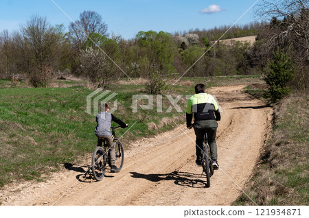 Father and son enjoy a sunny bike ride along a scenic country path. 121934871