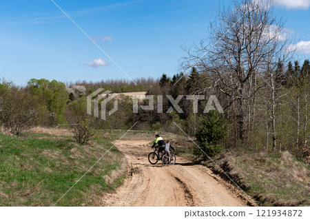 Two cyclists enjoy a scenic country road ride, surrounded by lush greenery and a tranquil atmosphere. Two cyclists enjoy a scenic country road ride, surrounded by lush greenery and a tranquil atmosphere. 121934872
