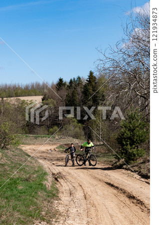 Father and son biking on a dirt road, enjoying a sunny day outdoors. A beautiful spring day. Father and son biking on a dirt road, enjoying a sunny day outdoors. A beautiful spring day. 121934873