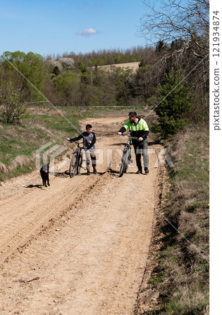 Father and son bike ride on a dirt road with their dog. Father and son bike ride on a dirt road with their dog. 121934874