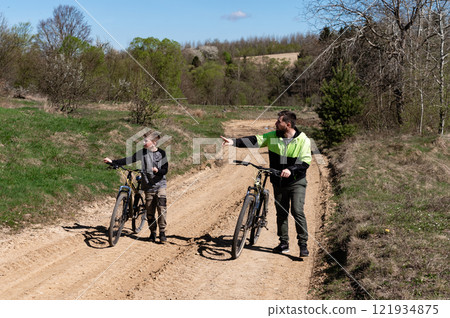 Father and son biking on a sunny day, enjoying a scenic countryside trail. Father and son biking on a sunny day, enjoying a scenic countryside trail. 121934875