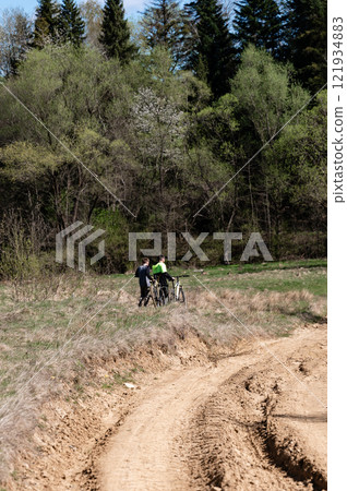 Two cyclists pause on a dirt path, enjoying the spring scenery. Two cyclists pause on a dirt path, enjoying the spring scenery. 121934883